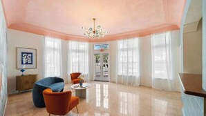 A spacious room with a polished floor, a blue sofa, an orange armchair, and a chandelier. - #02 Unit in Mid-century Art-Déco Building KingBed EnSuiteBath Steps>Beach PetsOK (Miami Beach)