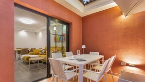 Un espace repas avec une table et des chaises blanches, une cloison en verre et une vue sur un salon comprenant un canapé et des fauteuils.