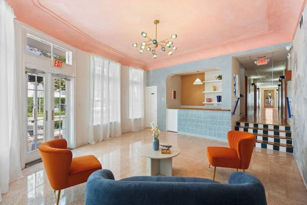 A lobby with a reception desk, two orange armchairs, a blue sofa, and a chandelier.