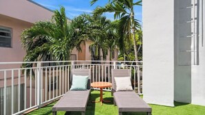 Ein Balkon mit zwei Liegestühlen, einem kleinen runden Tisch und einem weißen Geländer.