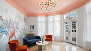 Eine Hotelhalle mit einem blauen Sofa, orangefarbenen Sesseln, einem Couchtisch und einem Wandbild mit tropischen Vögeln.