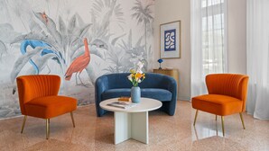 A room with a blue sofa, two orange armchairs, a white coffee table, and a wall mural with tropical birds and plants. - #04 Corner Unit in Mid-century Art-Déco building KingBed EnSuiteBath PetsOK (Miami Beach)