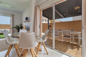 Moderni ruokailutila, jossa on lasipöytä, valkoiset tuolit ja näkymä ulkoterasille.