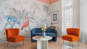 A room with two orange armchairs, a blue sofa, and a white coffee table. There is a tropical mural on the wall and a framed artwork above the sofa. - #07 Corner Unit in Mid-century Art-Déco building KingBed EnSuiteBath PetsOK (Miami Beach)