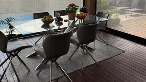 Un espace de salle à manger moderne, avec une table et des chaises en verre, donnant sur une cour intérieure et doté d’une grande fenêtre.