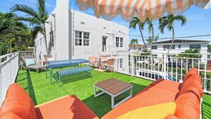A white building with a fenced patio area, outdoor seating, and palm trees. - #09 2B-2B Unit in Art-Déco Building KingBed freeCarSpace! Kitchen PetsOK (Miami Beach)