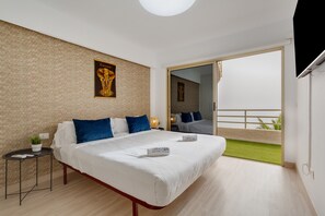 A bedroom with a bed, a small table with a plant, a wall-mounted picture, and a balcony with a view.