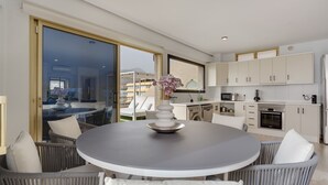 A modern kitchen with white cabinets, a dining area with wicker chairs, and a large window. - Vacation Apartment 'Obsidian Mirador Oceano' with Sea View, Wi-Fi and Air Conditioning (Puerto de Santiago)