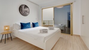 A modern bedroom with a bed, pillows, a bedside table, a wall-mounted picture, and a sliding glass door leading to a balcony. - Vacation Apartment 'Obsidian Mirador Oceano' with Sea View, Wi-Fi and Air Conditioning (Puerto de Santiago)