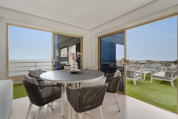 A balcony with a round table and chairs, a small indoor area with a view, and a grassy outdoor area.