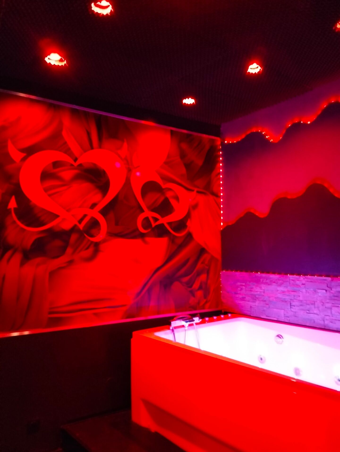 A room with a red-lit wall, a bathtub, and a stone wall.