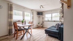 A modern living room with a dining table, a sofa, and a TV mounted on the wall. - Apartment 'Rebblick' with Shared Terrace, Shared Garden and Wi-Fi (Oberkirch)