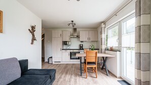 A modern kitchen with wooden cabinets, a dining table with a chair, and a sofa in a living area. - Apartment 'Rebblick' with Shared Terrace, Shared Garden and Wi-Fi (Oberkirch)