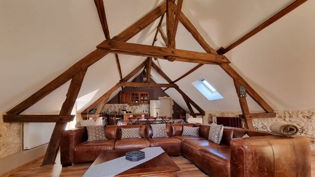 A loft-style living space with a wooden ceiling structure, a brown leather sectional sofa, a wooden coffee table, and a stone wall. - Les Granges Indigo (Fossemagne)