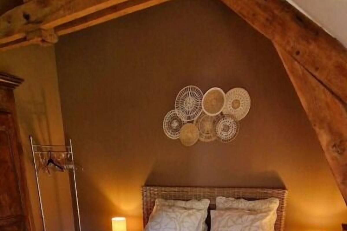 A cozy bedroom with a wooden ceiling, a bed with a patterned bedspread, two bedside lamps, and a wall decor piece.