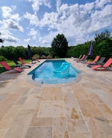 A rectangular swimming pool with a tiled deck, surrounded by lounge chairs and umbrellas.