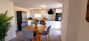 A modern kitchen with a dining area, featuring a central island, chairs, and a potted plant.