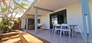 A covered outdoor area with a wooden deck, white chairs, a hanging chair, and a sofa.