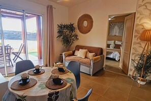 A dining area with a table set for two, a sofa, and a large plant.