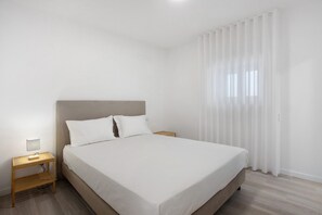 Ein Schlafzimmer mit Bett, Nachttisch, Lampe und einem Fenster mit Vorhängen.