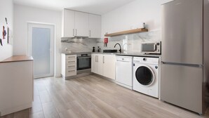 A modern kitchen with a built-in oven, microwave, washing machine, and a stainless steel refrigerator.