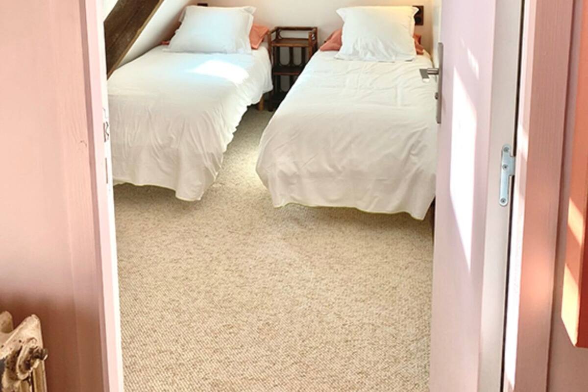 A bedroom with two beds, a sloped ceiling, and a wooden beam structure.