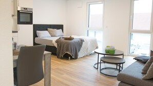 A modern, well-lit room with a bed, a dining area, and a small table. - Boardinghouse Baumhof 55 (Marktheidenfeld)