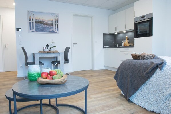 A modern apartment with a dining area, kitchenette, and a cozy seating area with a blanket. - Boardinghouse Baumhof 55 (Marktheidenfeld)