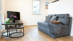 A modern living room with a grey sofa, a small round table with decorative items, and a flat-screen TV. - Boardinghouse Baumhof 55 (Marktheidenfeld)