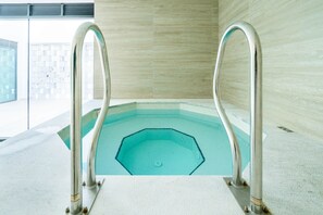 A clear view of a swimming pool with two metal ladders, a tiled floor, and a tiled wall in the background.