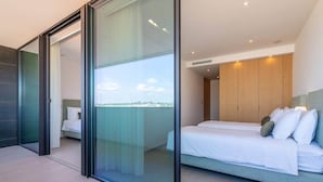 Et moderne soveværelse med en stor skydedør til en balkon, en seng med hvide sengetæpper og en træsenggavl.