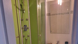 A bathroom with a glass-enclosed shower, a white sink, and a mirror above it. - La Tanière de Bains - F1 RDC (LA VOGE LES BAINS)