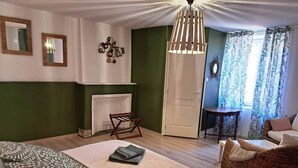 A bedroom with a bed, a chair, a table, a fireplace, and a door. - La Tani ère de Bains - F1 RDC (LA VOGE LES BAINS)