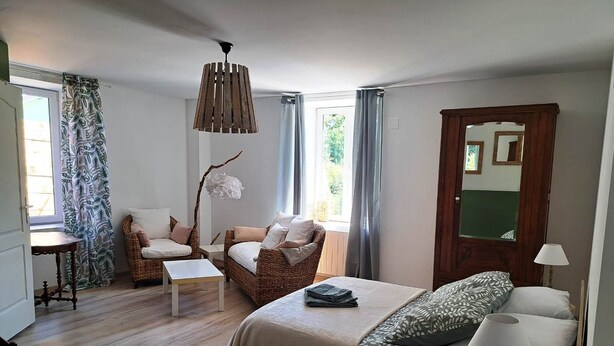 A bedroom with a bed, two chairs, a small table, a hanging light fixture, and a mirror on the wall. - La Tanière de Bains - F1 RDC (LA VOGE LES BAINS)