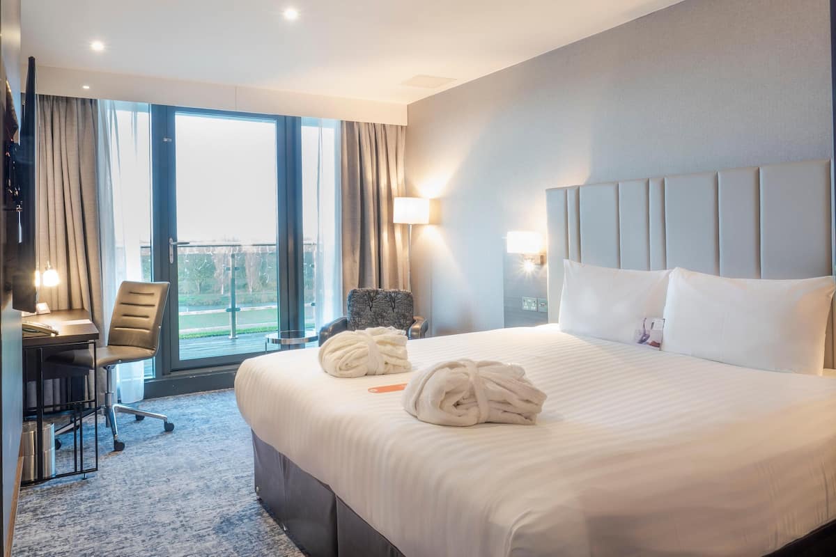 Una habitació d'hotel amb un llit, dues làmpades de nit, un escriptori amb una cadira, una finestra amb cortines i vista a l'exterior.