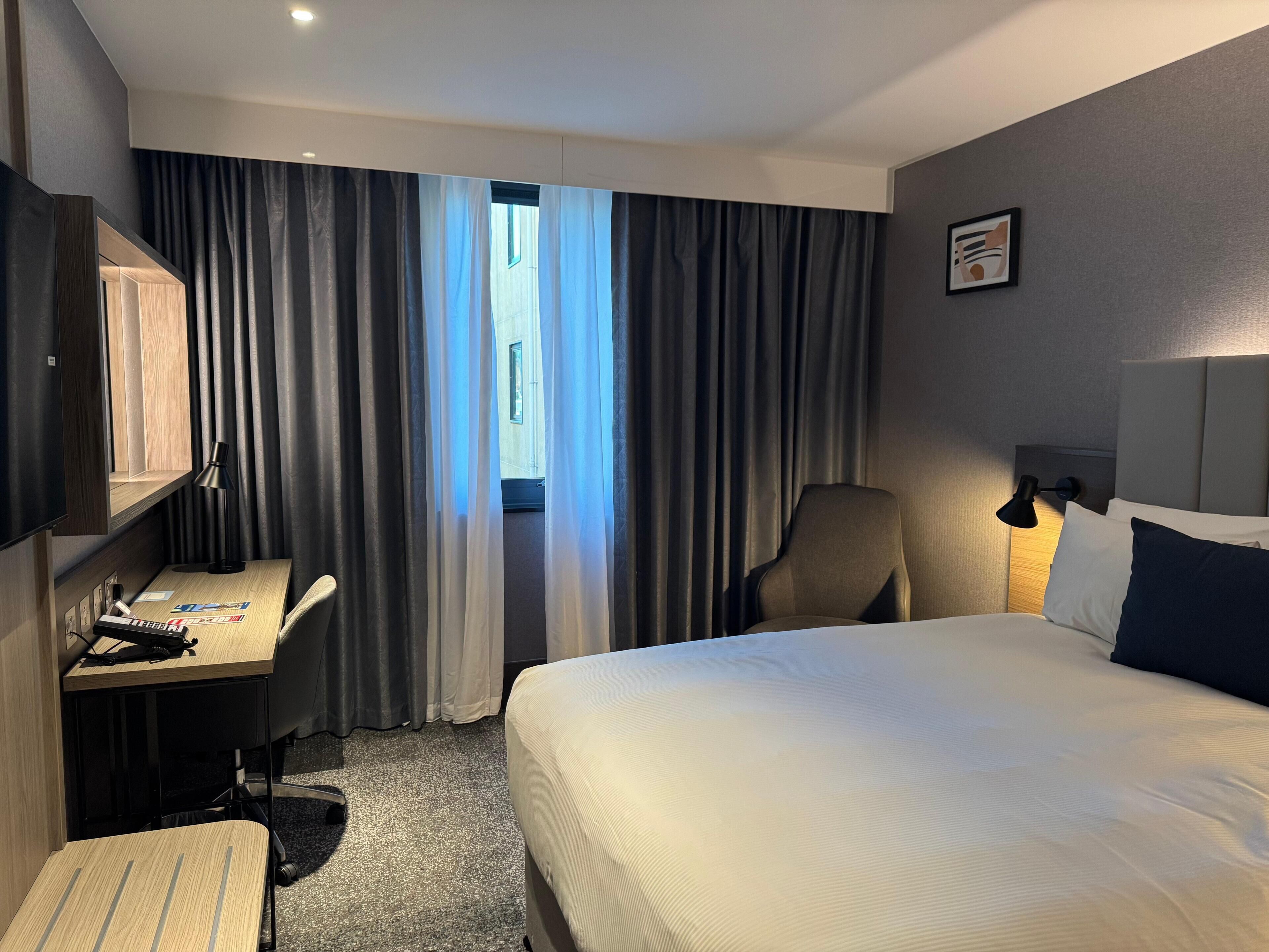A hotel room with a bed, desk, chair, and a television.
