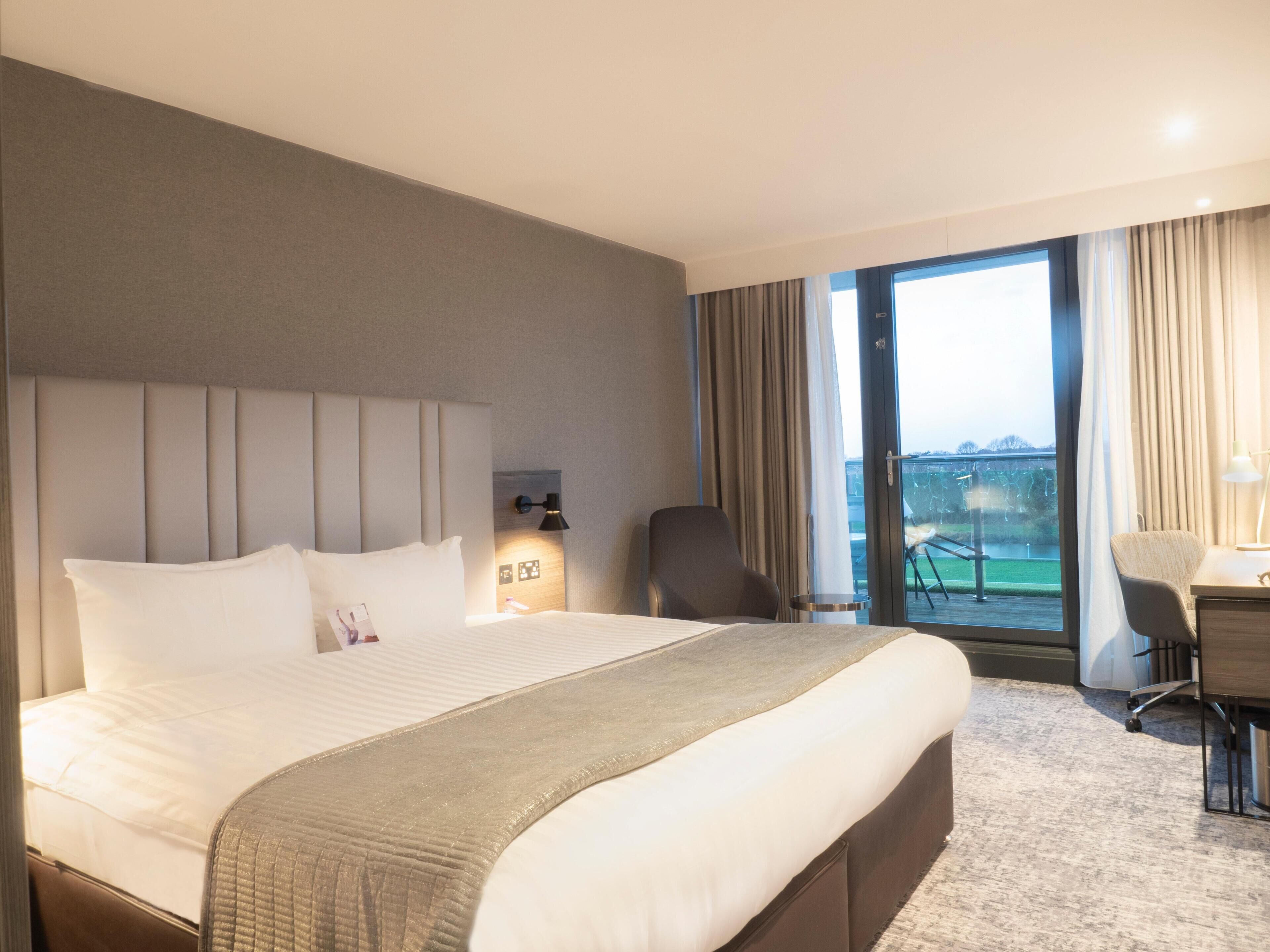 A hotel room with a large bed, a desk, a chair, and a view of the outdoors.