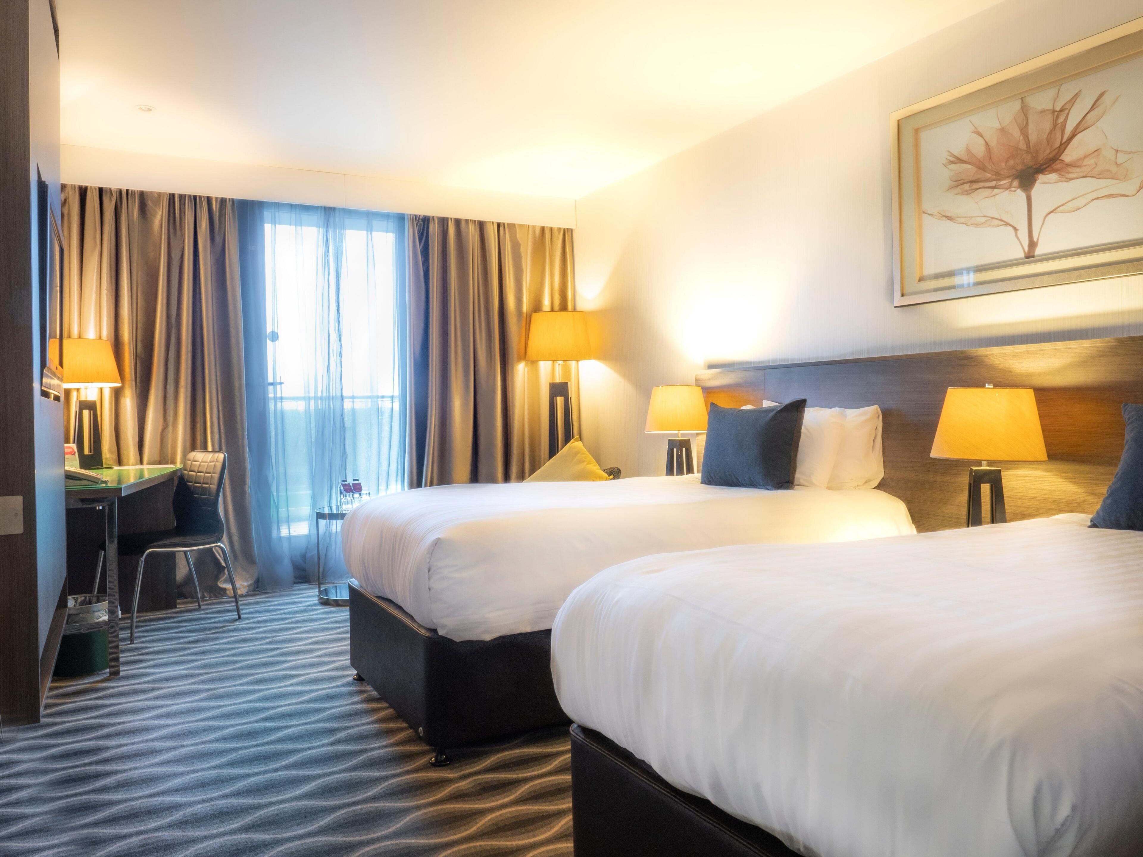A hotel room with two beds, a desk, and a chair.