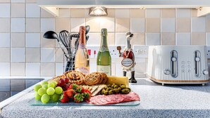Un plan de travail de cuisine sur lequel on trouve une variété d’aliments, notamment des raisins, des fraises, du fromage et de la viande, ainsi que des bouteilles de vin et un grille-pain.
