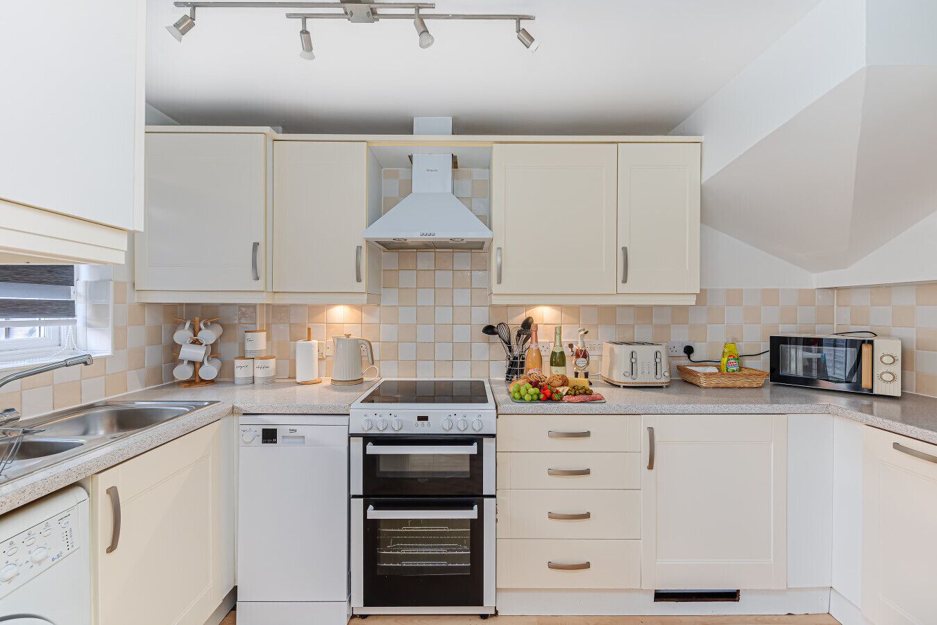 Een moderne keuken met witte kastjes, een ingebouwde oven, een magnetron en een koffieapparaat.