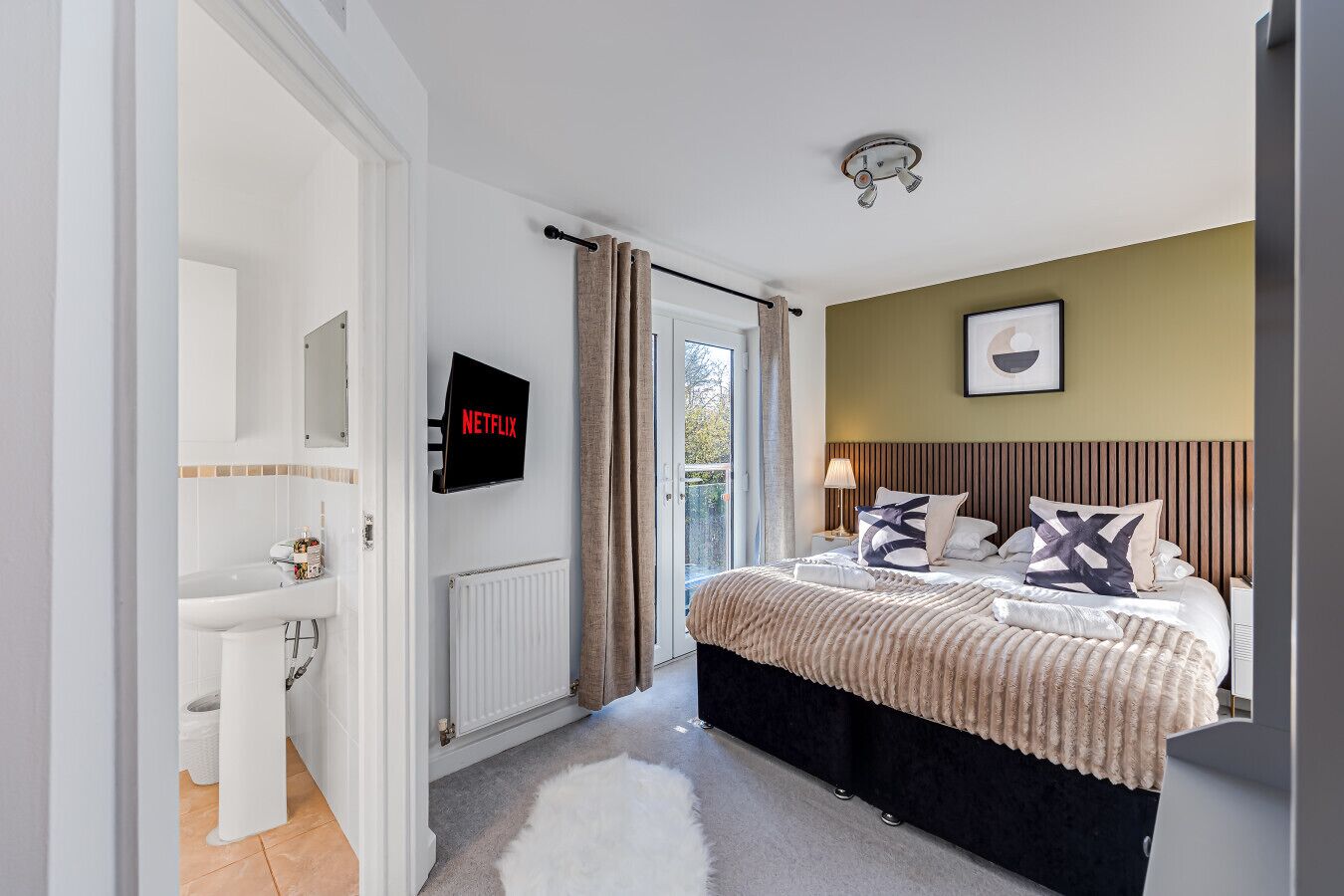 Ein Schlafzimmer mit Bett, Fernseher, Bad und Blick ins Freie.
