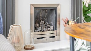 Ein modernes Wohnzimmer mit Kamin, einer gewebten Lampe und einem runden Tisch mit Blumen.