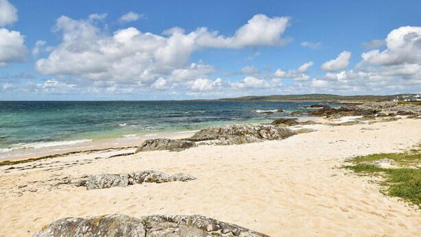A beach with clear skies, rocky shoreline, and distant buildings. - Mannin Lodge by Connemara Shores (Ballyconneely)