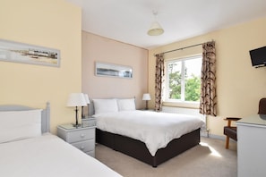 A bedroom with a bed, bedside tables, lamps, a window with curtains, and a television on the wall.