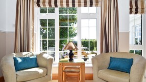 A room with two beige armchairs, a small wooden table, and a window with striped curtains. - Mannin Lodge by Connemara Shores (Ballyconneely)