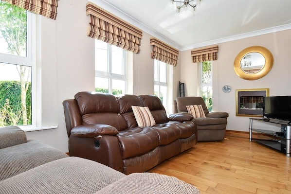 A living room with leather sofas, a television, and large windows with curtains.
