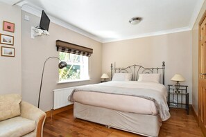 A bedroom with a bed, bedside lamps, a window with blinds, a radiator, and a television mounted on the wall. - Mannin Lodge (Ballyconneely)