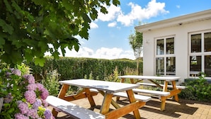 An outdoor patio area with picnic tables and a white building in the background. - Mannin Lodge by Connemara Shores (Ballyconneely)