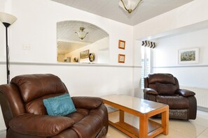A living room with two leather sofas, a glass coffee table, and a mirror on the wall. - Mannin Lodge (Ballyconneely)