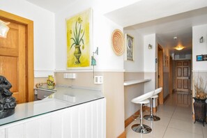 A modern kitchen with white cabinetry, a glass countertop, and a yellow vase with flowers.